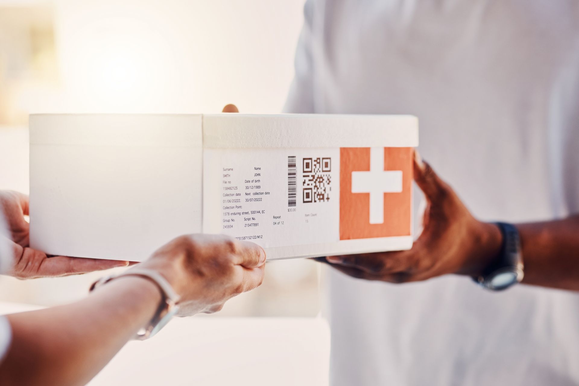 Delivery person hands a white box with a red cross logo to another person.