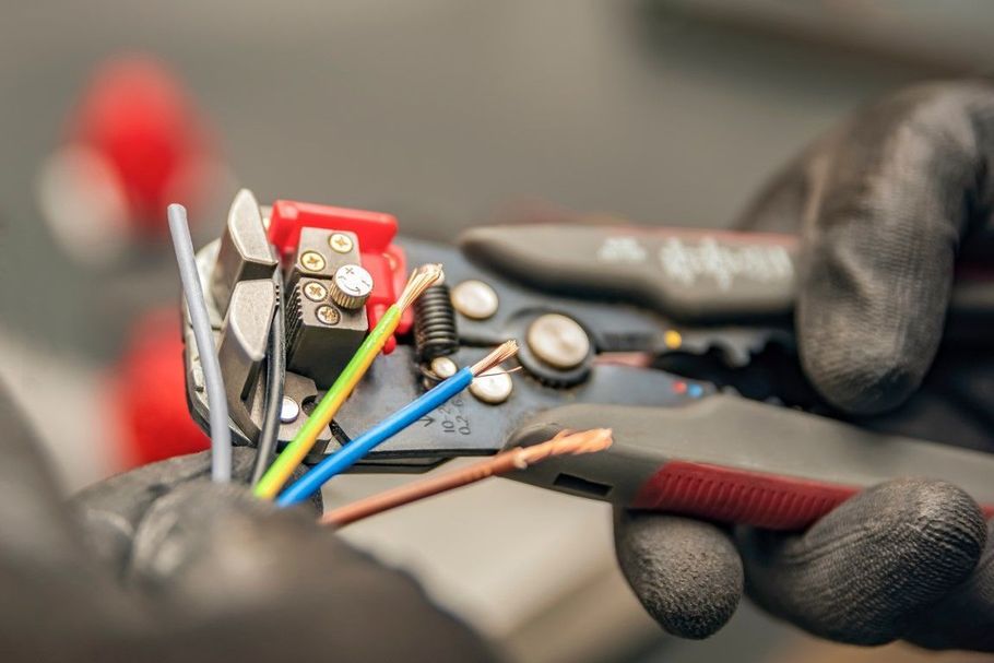 Gloved hands using wire cutters to strip colored electrical cables in a close-up repair scene