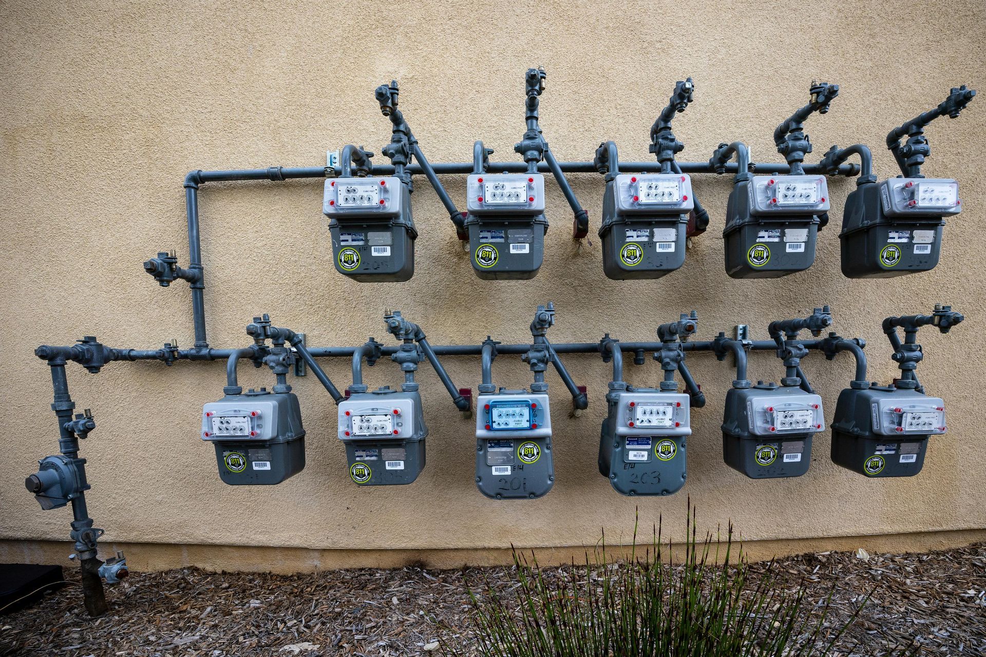Gas meters lined up on an exterior wall, connected by black pipes.