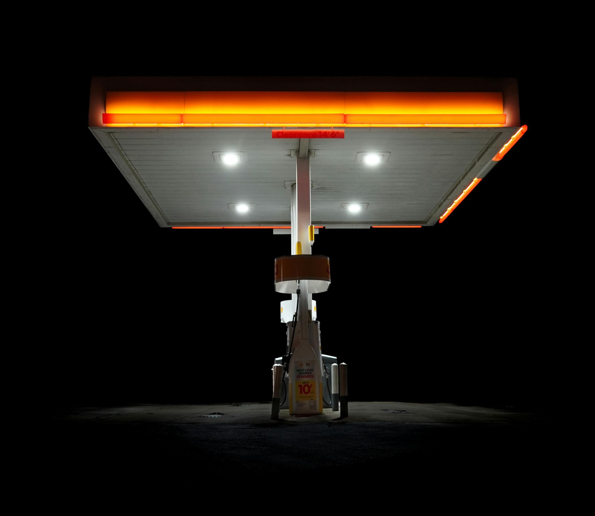 Lit gas station canopy against a black night sky; bright orange and white lights.