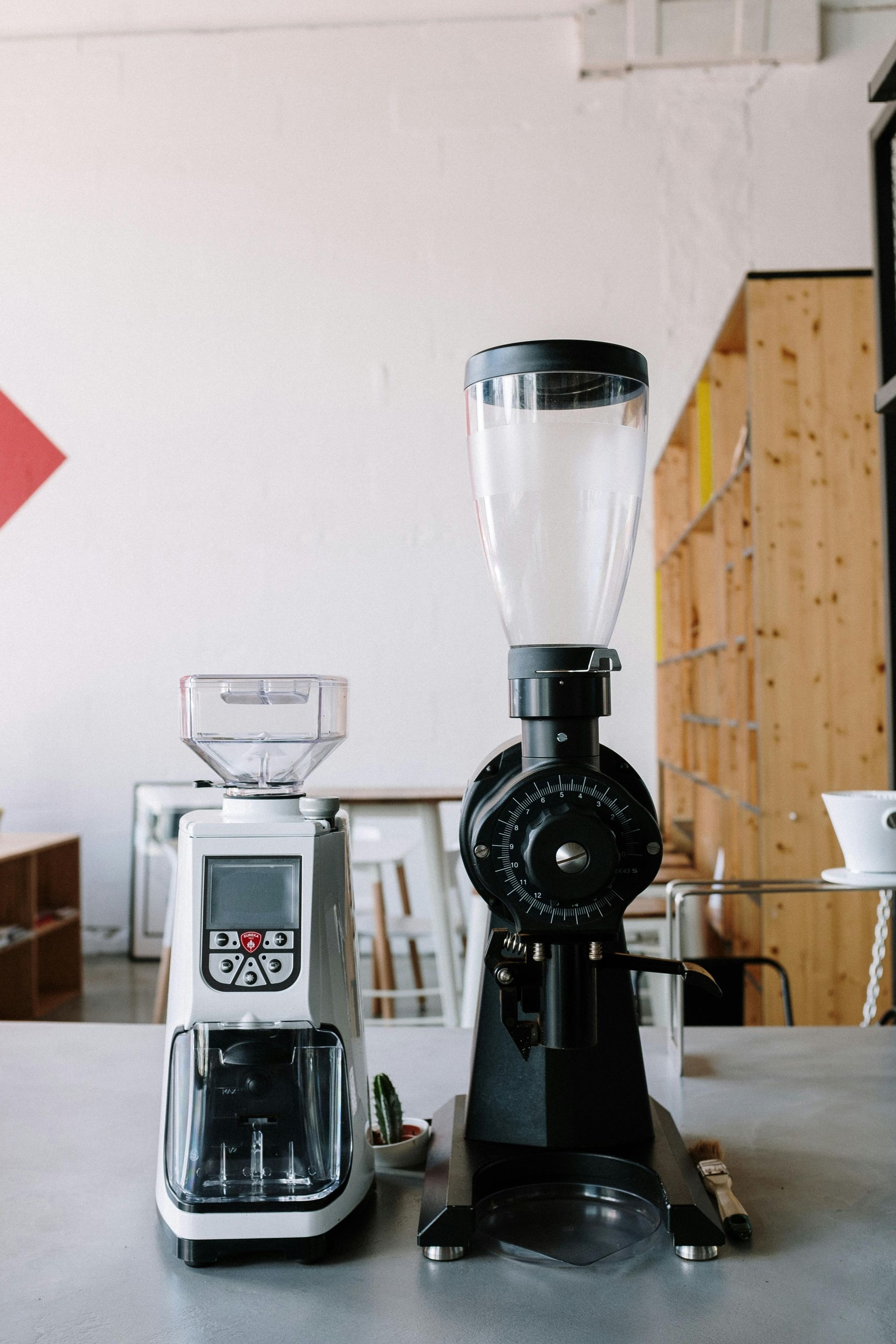 Two coffee grinders on a counter: a silver/black grinder on the left, and a black grinder with a clear hopper on the right.