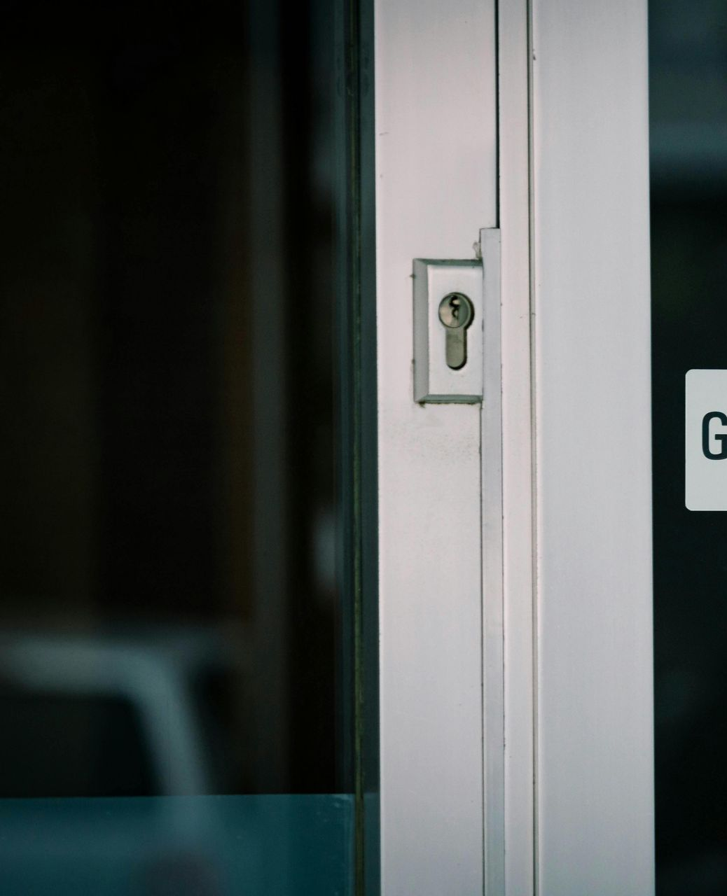 Keyhole on a glass door. The frame is white. The background is blurred.