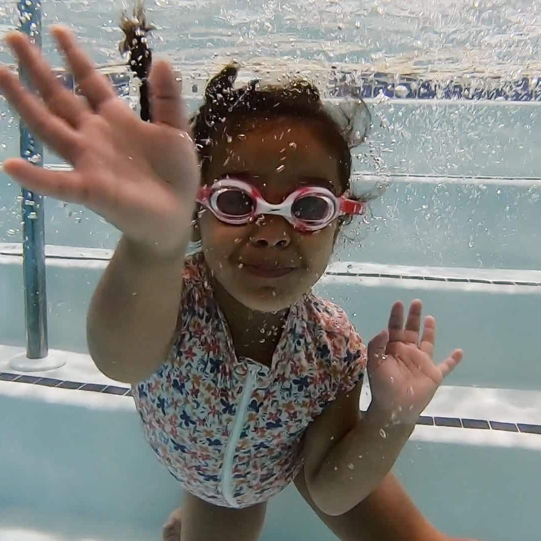 A little girl wearing goggles is swimming underwater