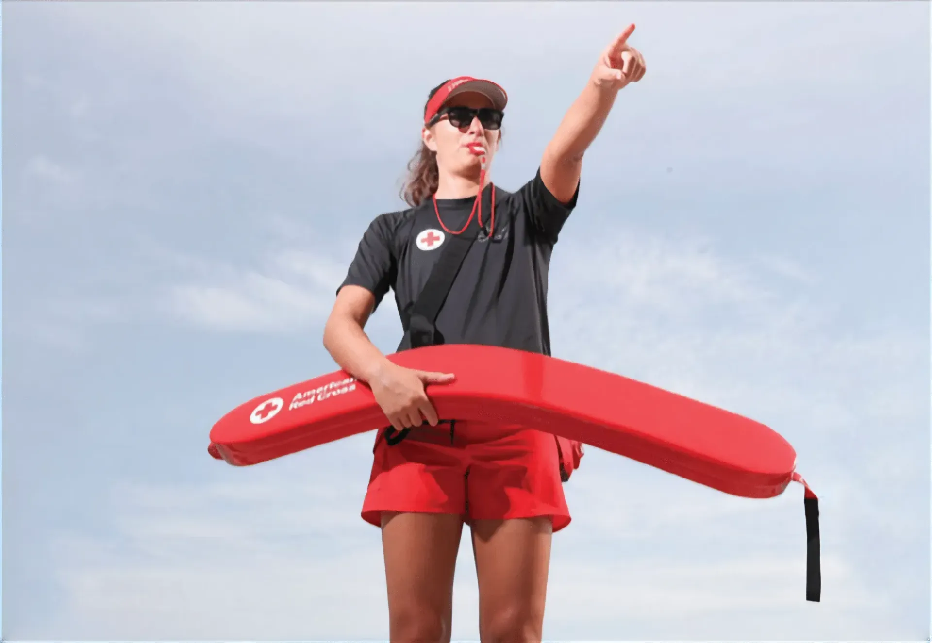 A lifeguard is holding a red life preserver and pointing at something.