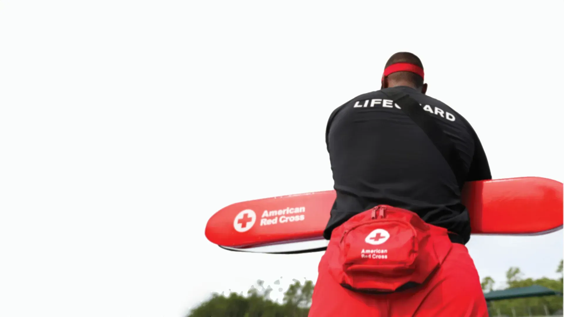 A lifeguard is holding a red life preserver on his back.