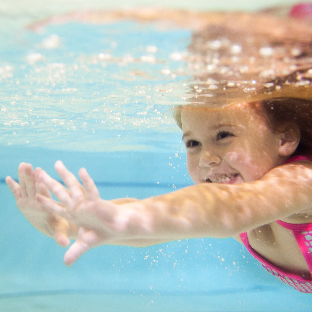 A little girl is swimming underwater in a swimming pool.