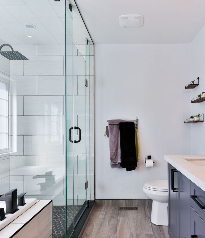 Modern bathroom with glass shower, white walls, and wood-look flooring.