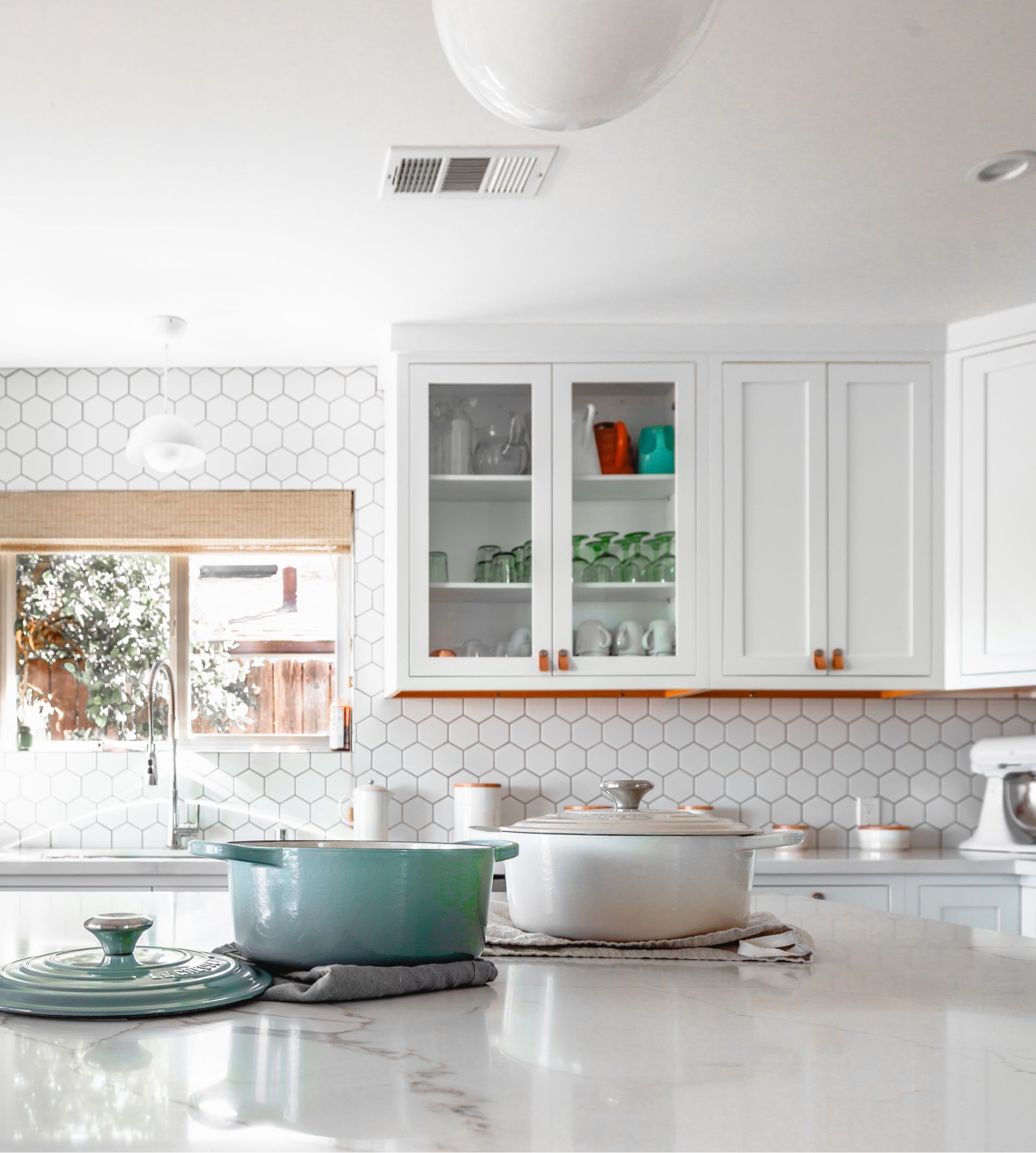 A kitchen with white cabinets , marble counter tops , pots and pans on the counter.