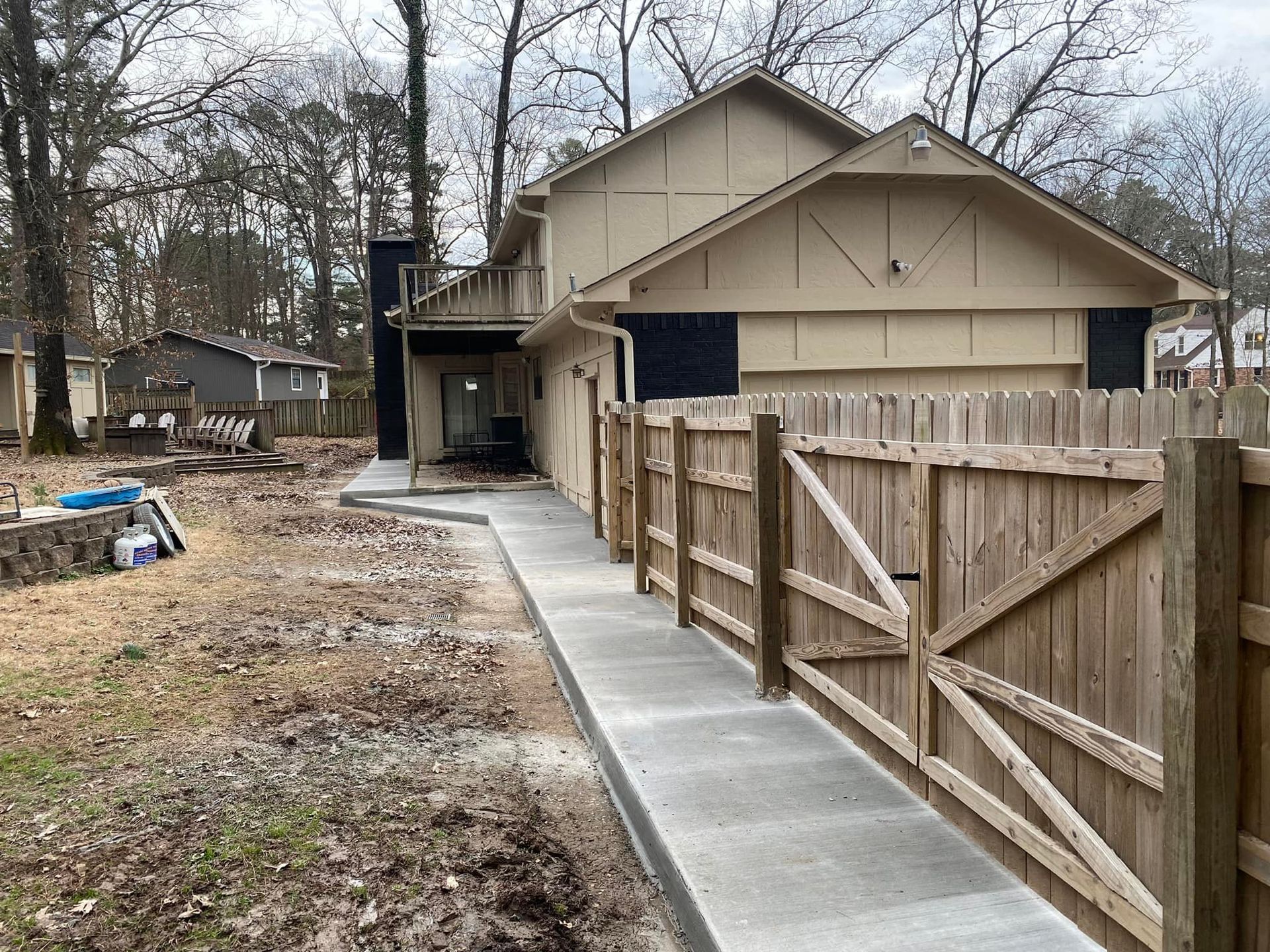 A house with a wooden fence and a concrete walkway leading to it.