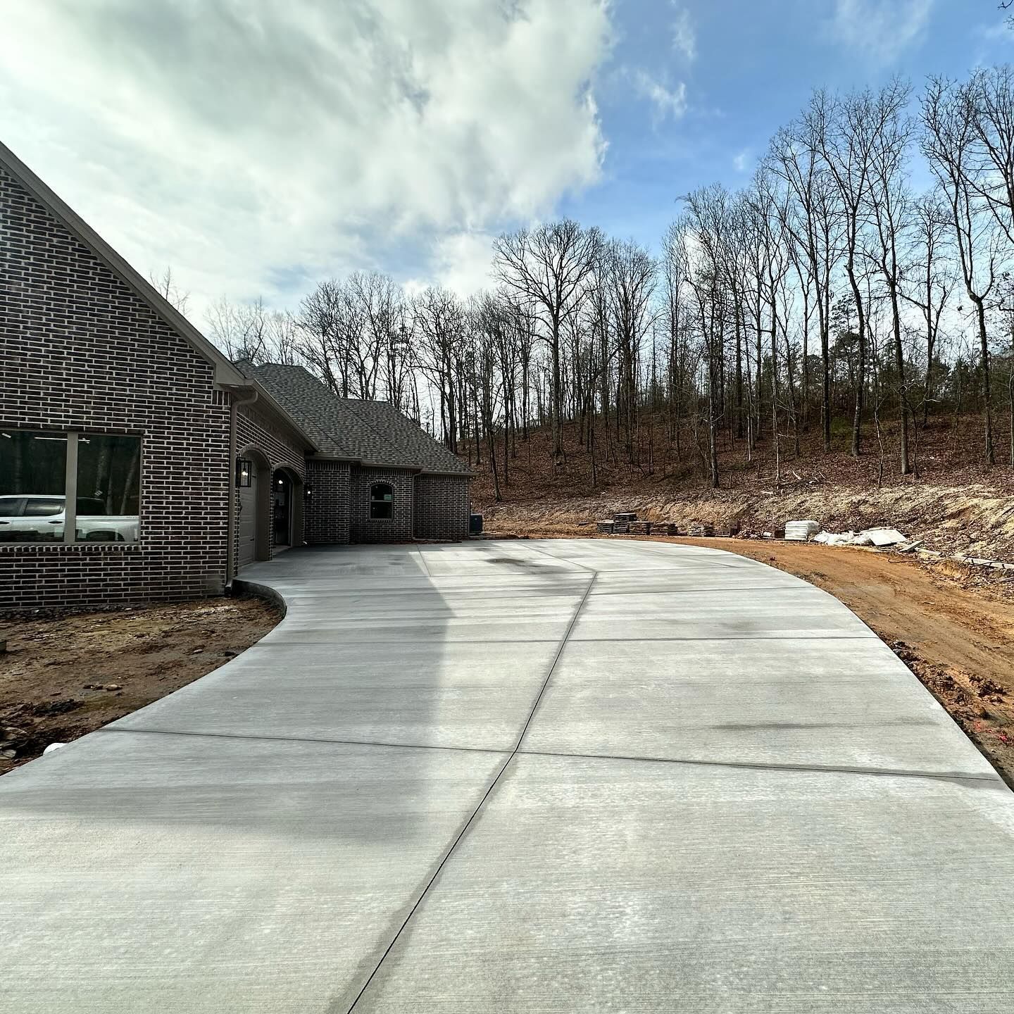 A concrete driveway leading to a house with trees in the background.