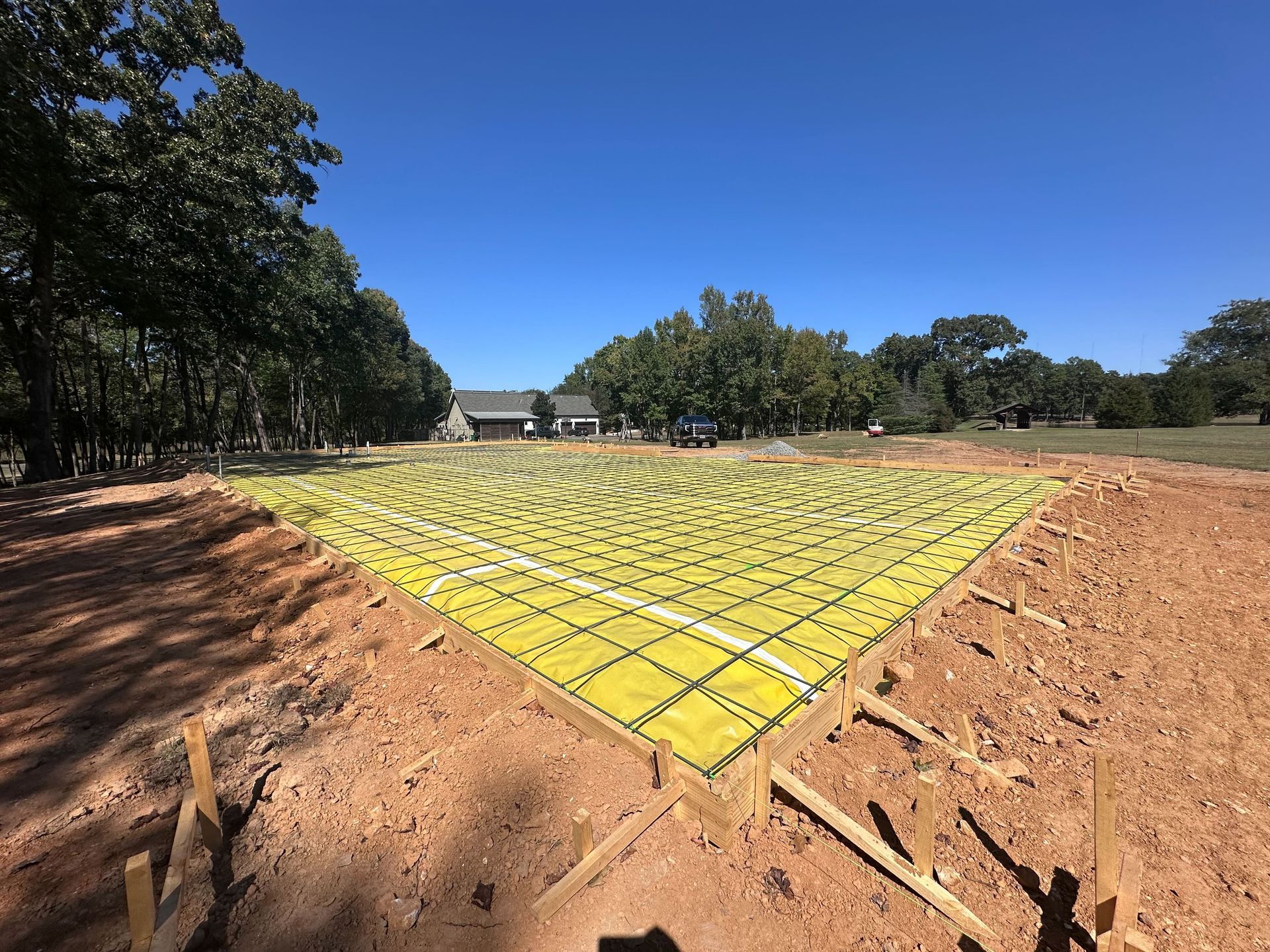 A concrete foundation is being built in a dirt field with a house in the background.