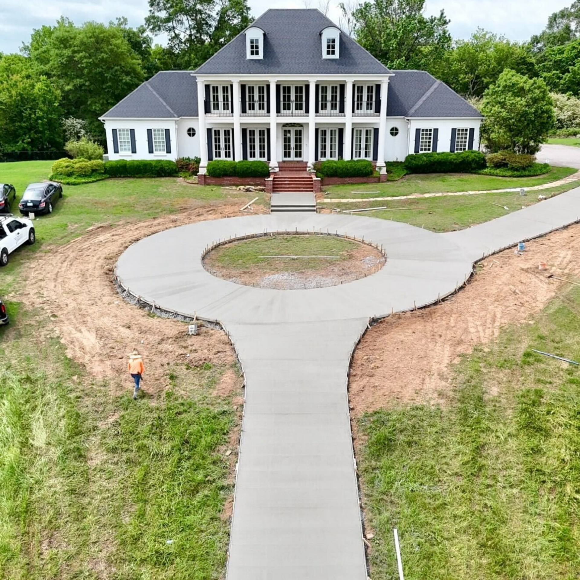 A concrete driveway leading to a house with trees in the background