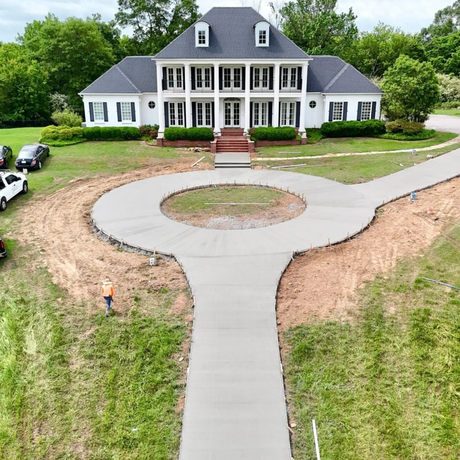 A concrete driveway leading to a house with trees in the background