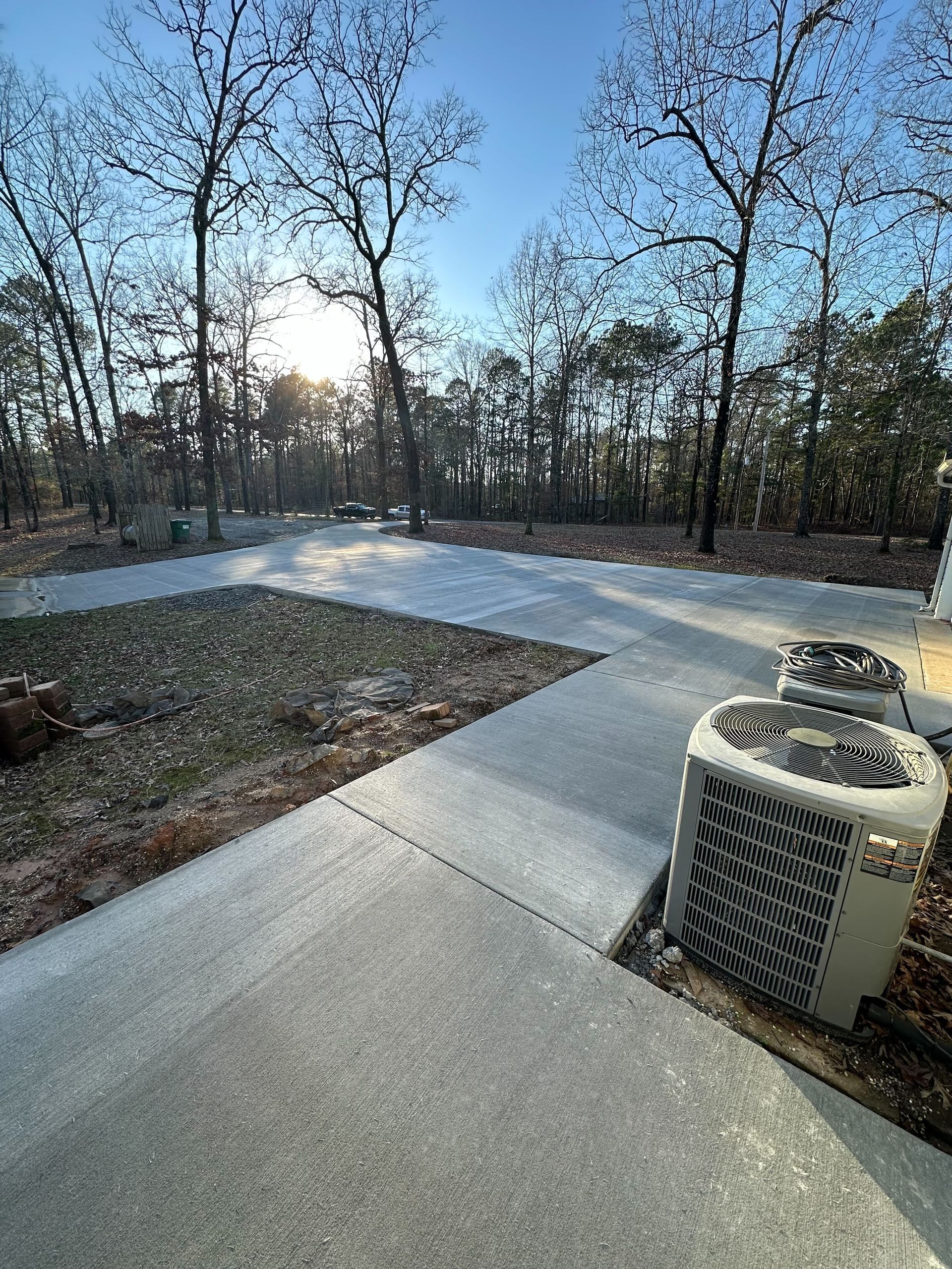 A concrete walkway with trees in the background and a couple of air conditioners on the side of it.