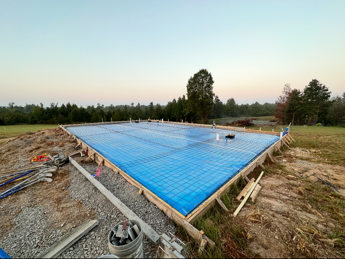 A blue tarp is covering a concrete foundation in a field.