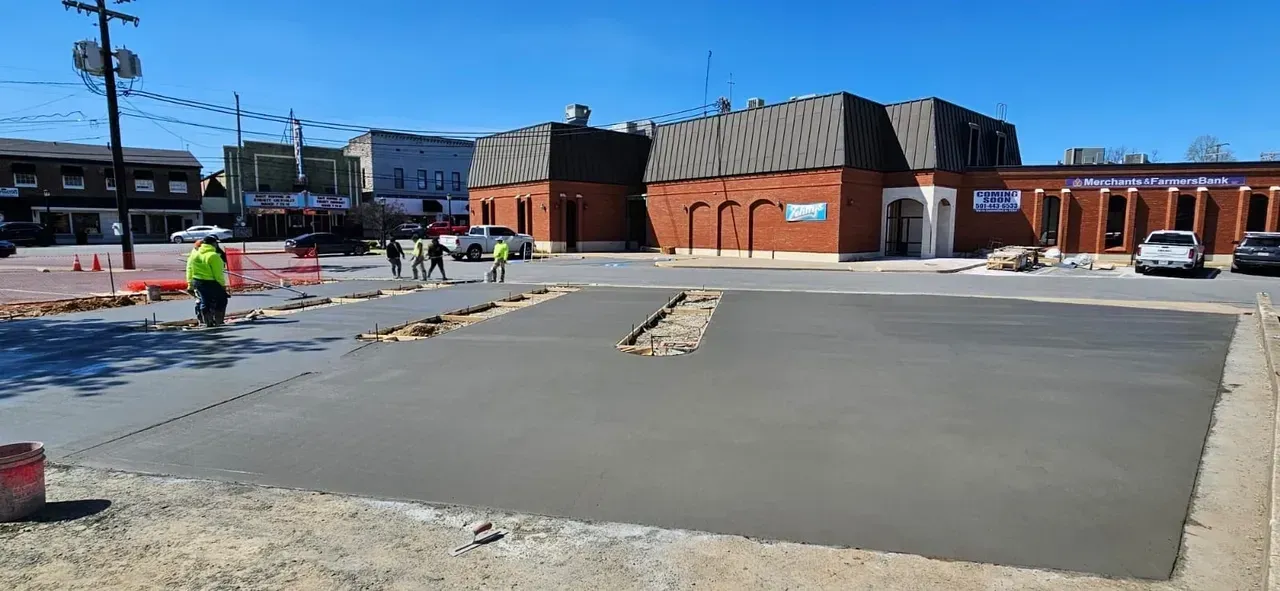 A group of construction workers are working on a concrete driveway in front of a building.