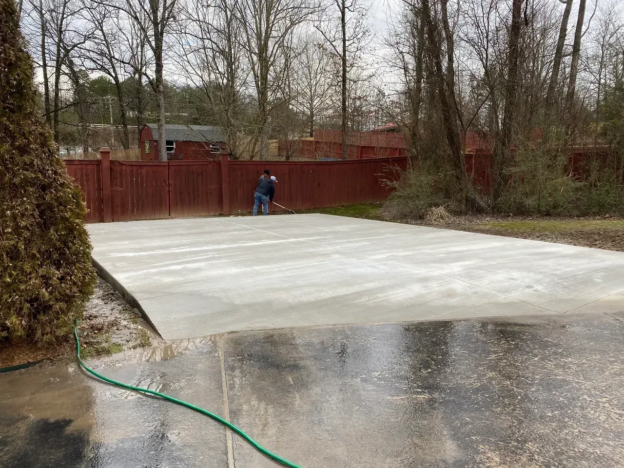 A man is standing on a concrete driveway next to a green hose.