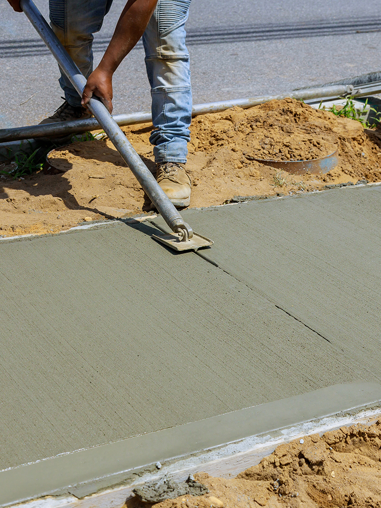 A man is spreading concrete on a sidewalk with a trowel.