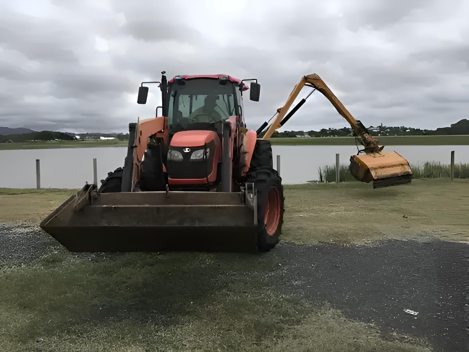 A Tractor With A Bucket Attached To It Is Parked Next To A Body Of Water — Cane Country Slashing & Mowing In Marian, QLD 