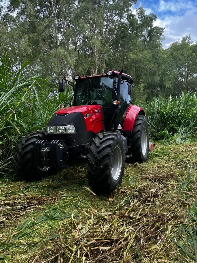 A Red Tractor Is Parked In A Field Of Tall Grass — Cane Country Slashing & Mowing In Marian, QLD
