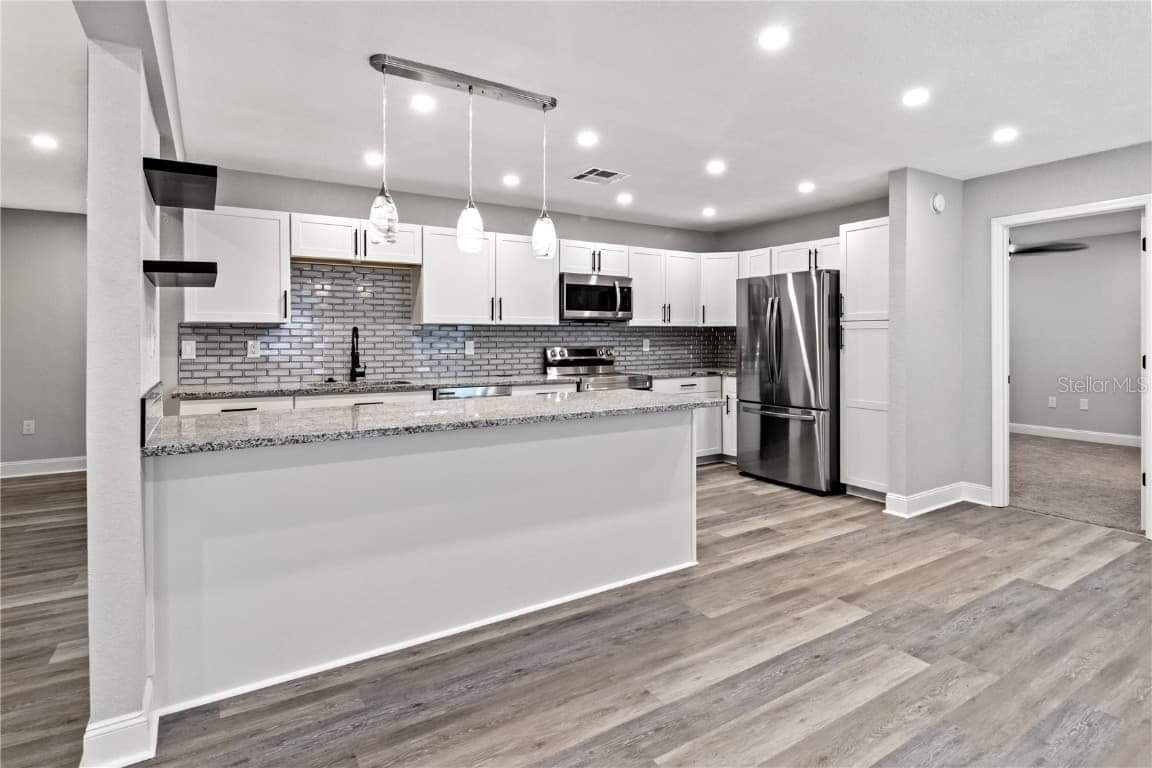 A kitchen with white cabinets , granite counter tops , stainless steel appliances and hardwood floors.