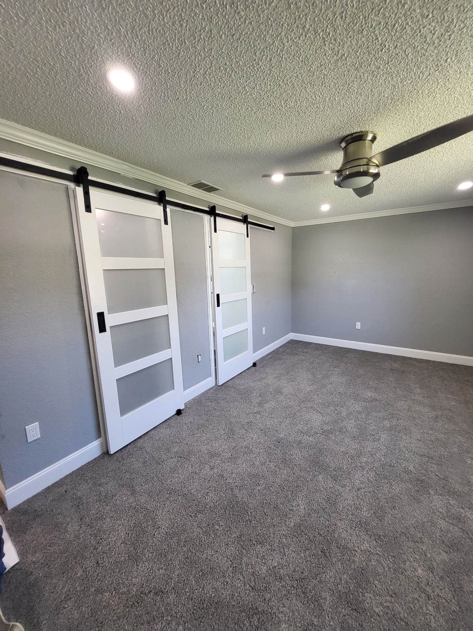 An empty room with sliding barn doors and a ceiling fan.
