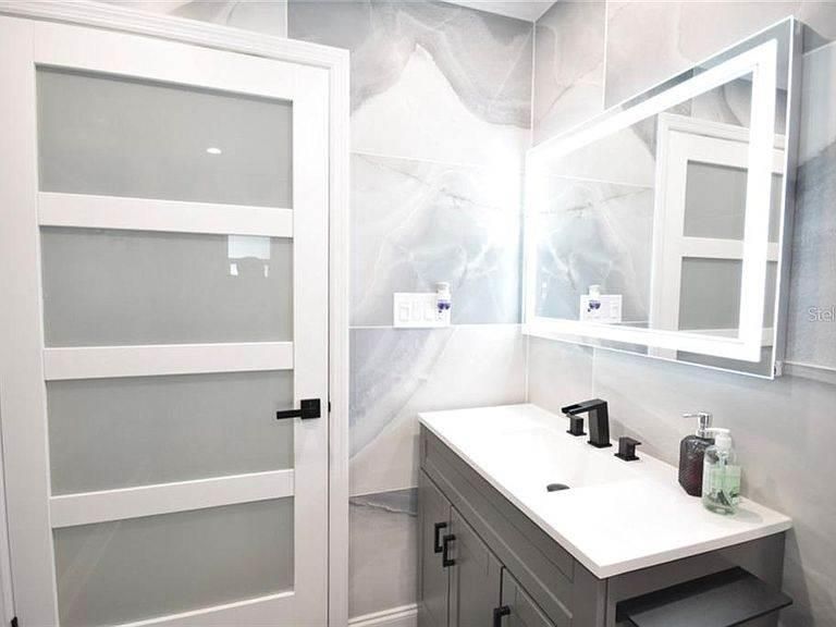 A bathroom with a sink , mirror and door.