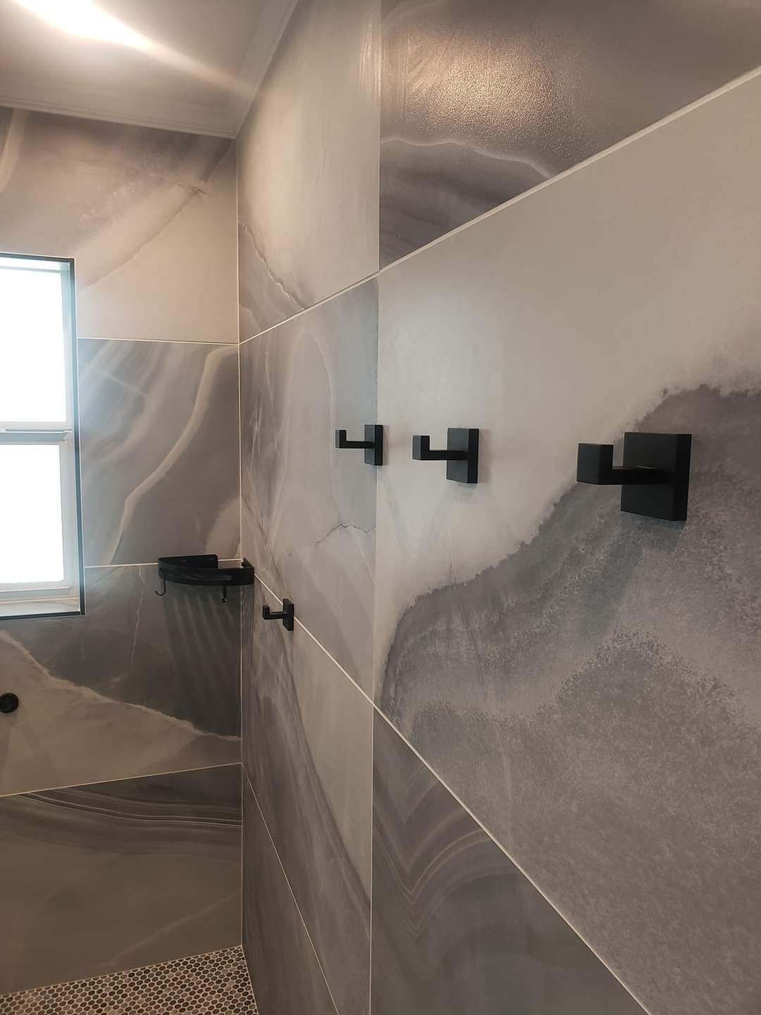 A bathroom with gray and white tiles and black hooks on the wall.