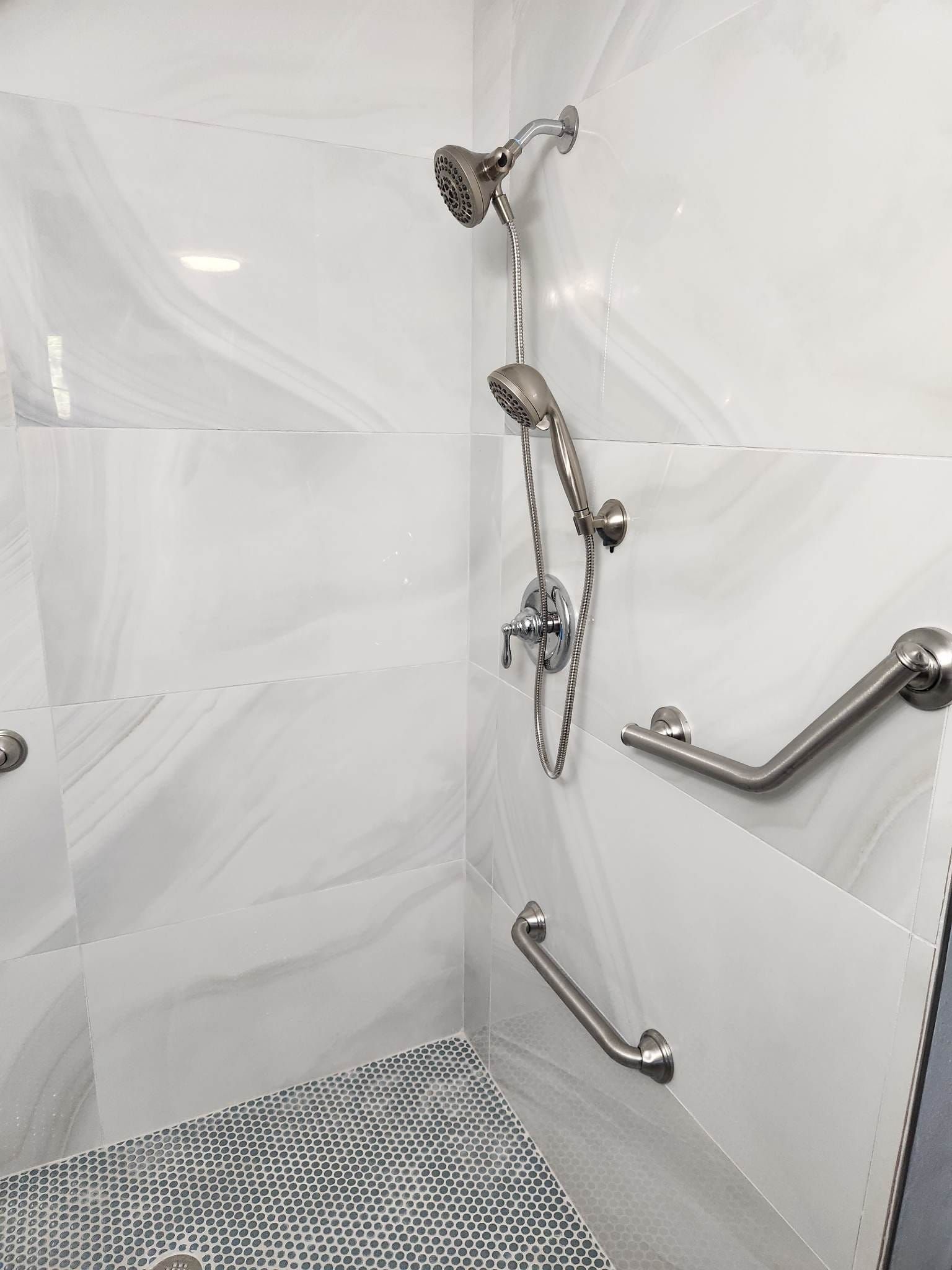 A bathroom with a walk in shower and stainless steel handles.