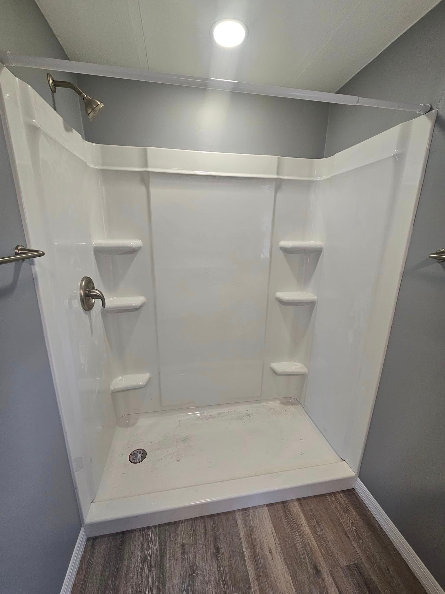 A white shower stall with shelves and a shower head in a bathroom.