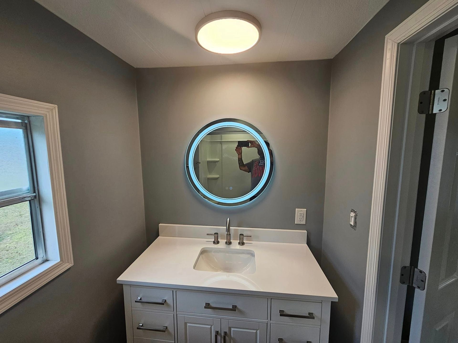 A bathroom with a sink , mirror and window.