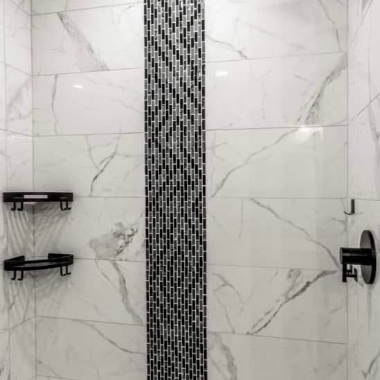 A shower with marble tiles and a black and white mosaic wall.