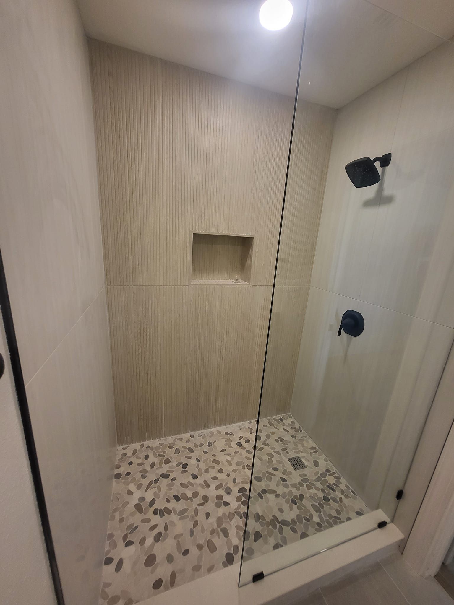A bathroom with a walk in shower with a glass door and a shower head.
