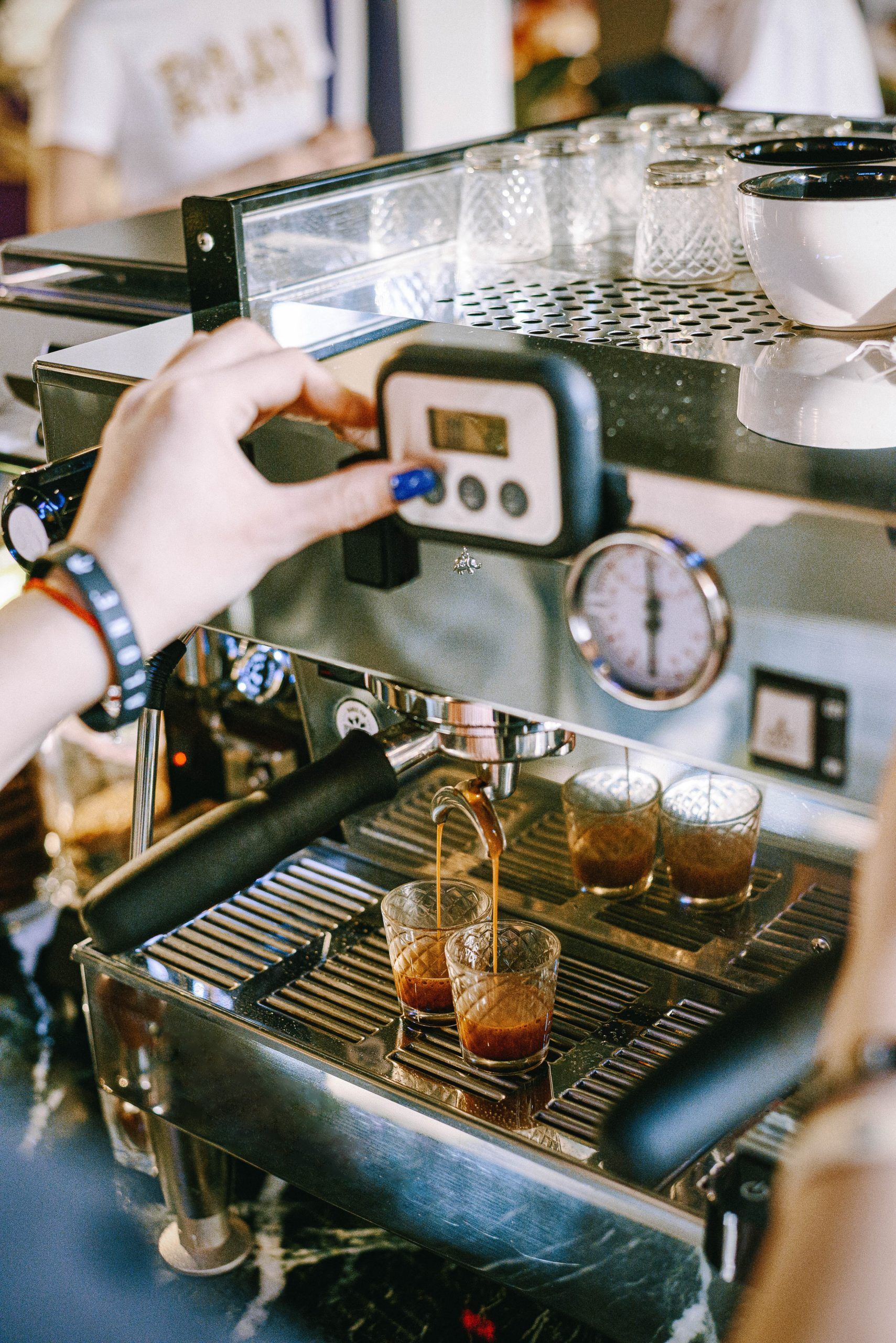 Person adjusts espresso machine, pouring shots into small glasses.
