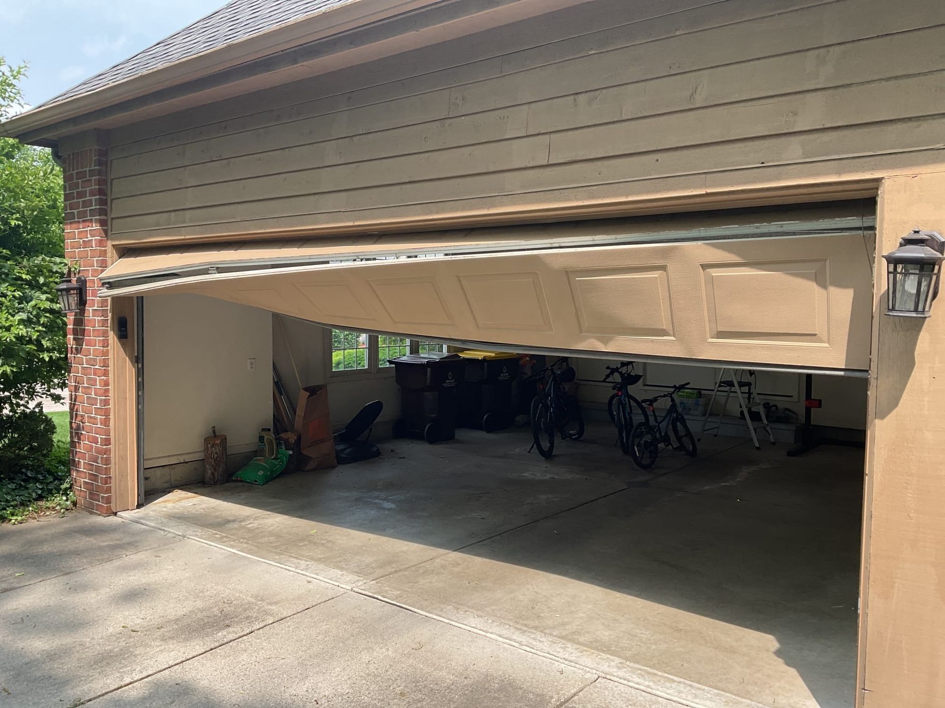Partially open garage with a white door, bicycles inside, and a concrete driveway in front.
