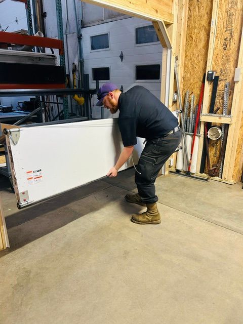 Man using a red drill to install a garage door bracket inside an unfinished garage Man using a red drill to install a garage door bracket inside an unfinished garage