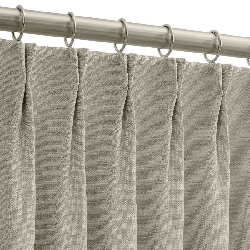 Light gray pleated curtain hanging from a silver rod with rings