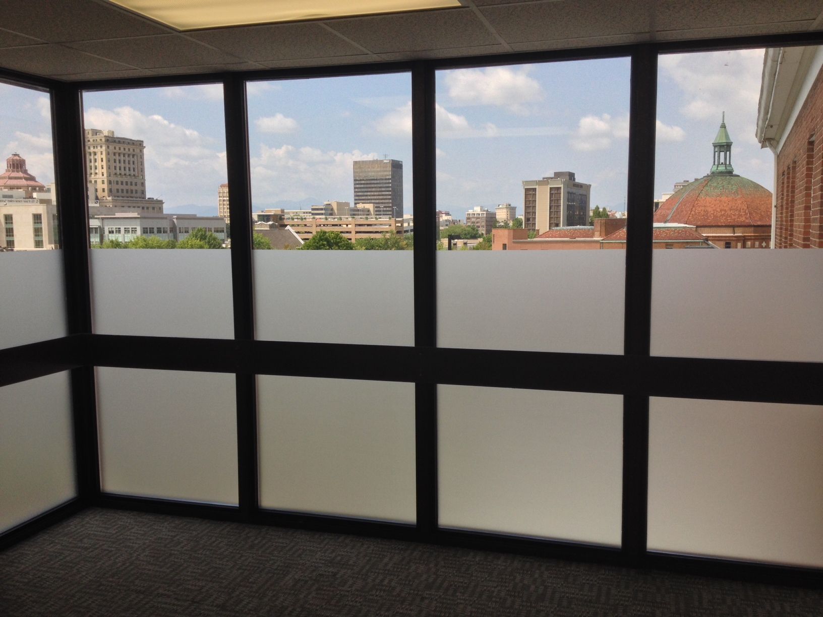 Office window view over a city skyline with buildings and a red domed roof under a cloudy sky