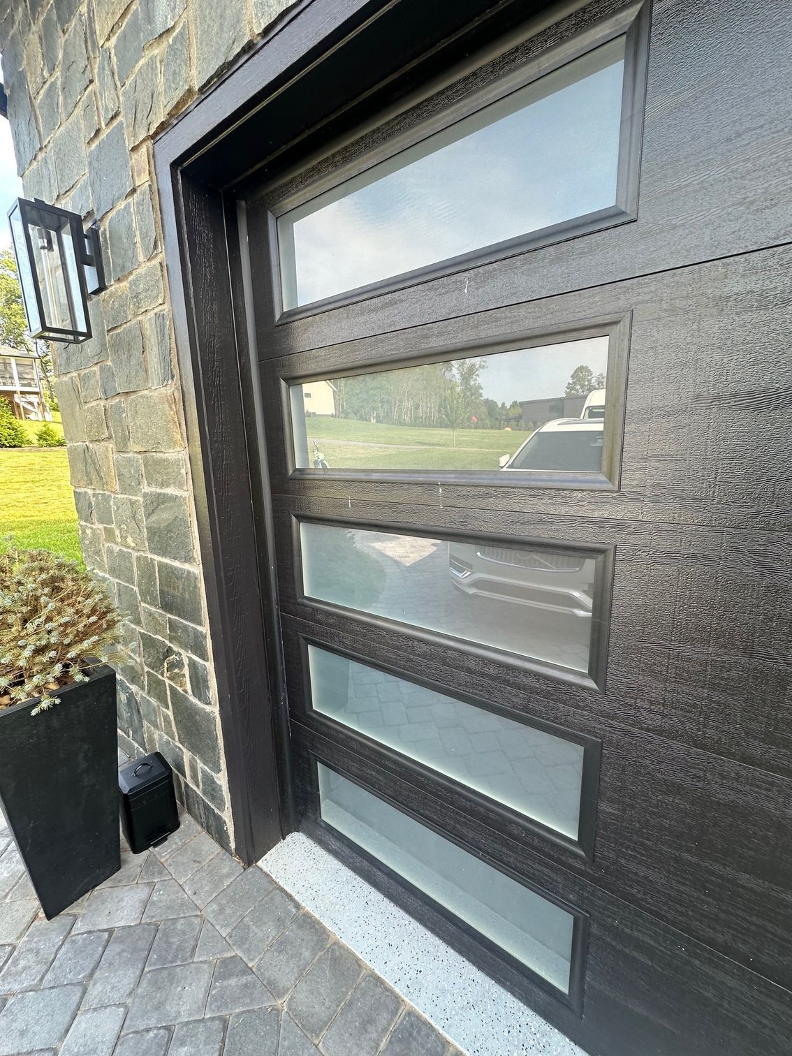 Modern black front door with frosted glass panels beside a stone wall and gray tiled entryway