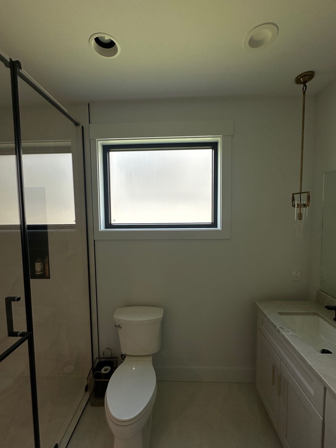 Small modern bathroom with a shower, toilet, sink, and frosted window