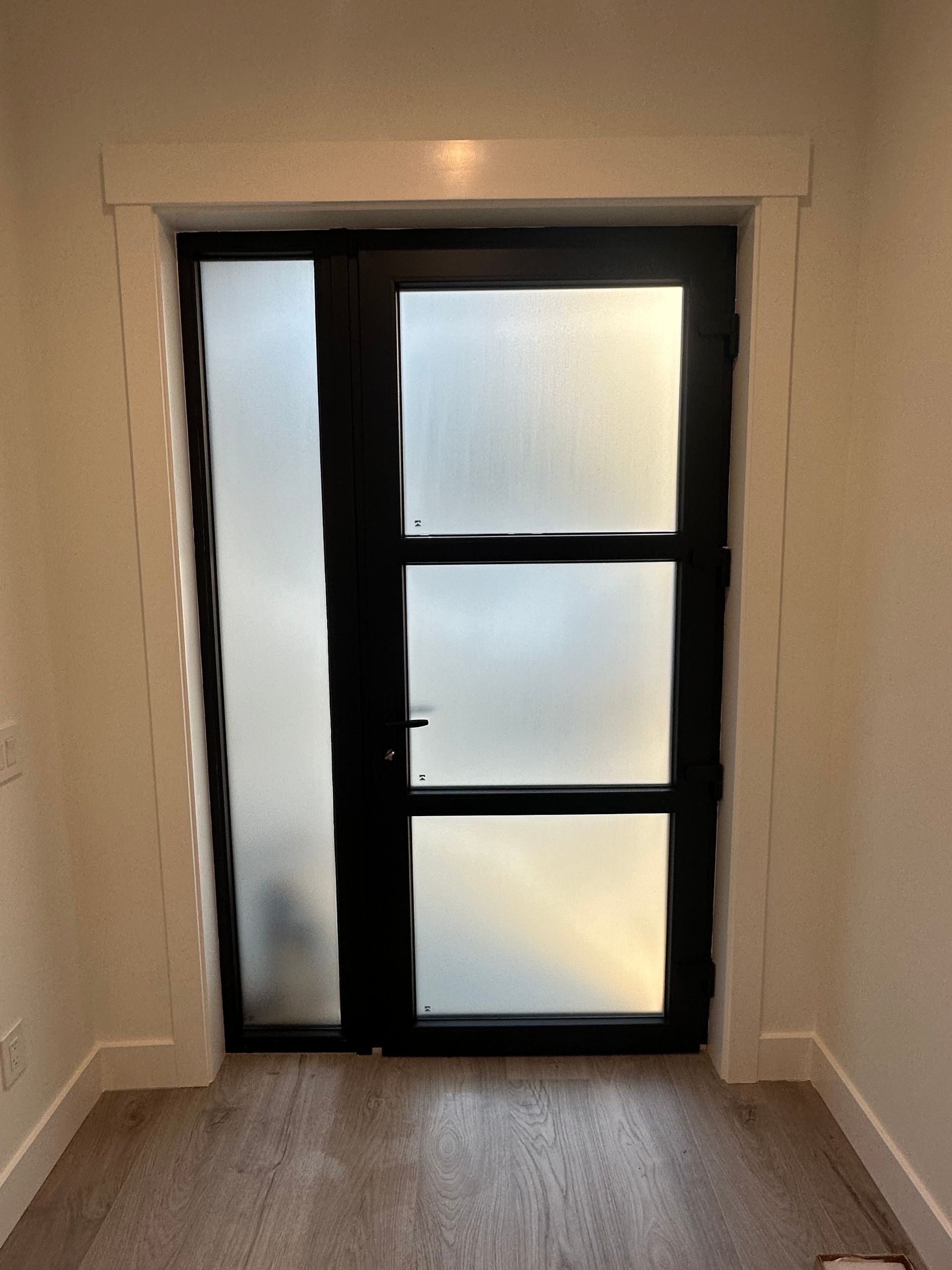Narrow entryway with a black-framed frosted glass door and wood floor.