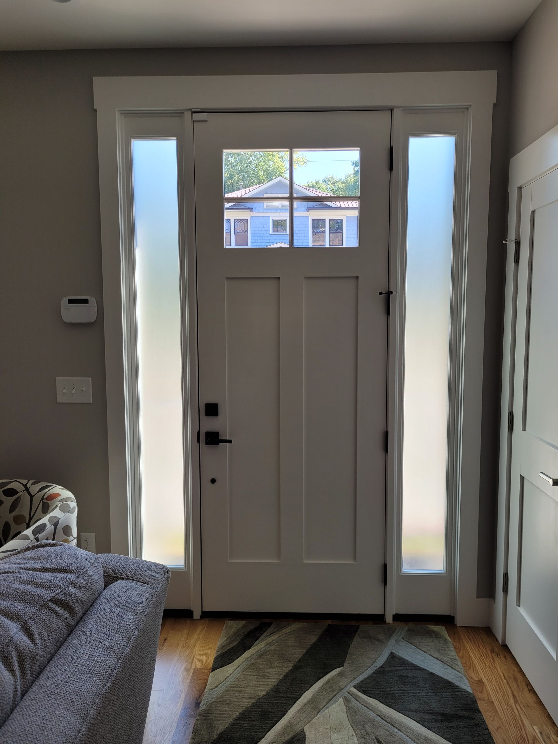 Front entryway with white door, narrow windows, striped rug, and partial view of a sofa on the left.