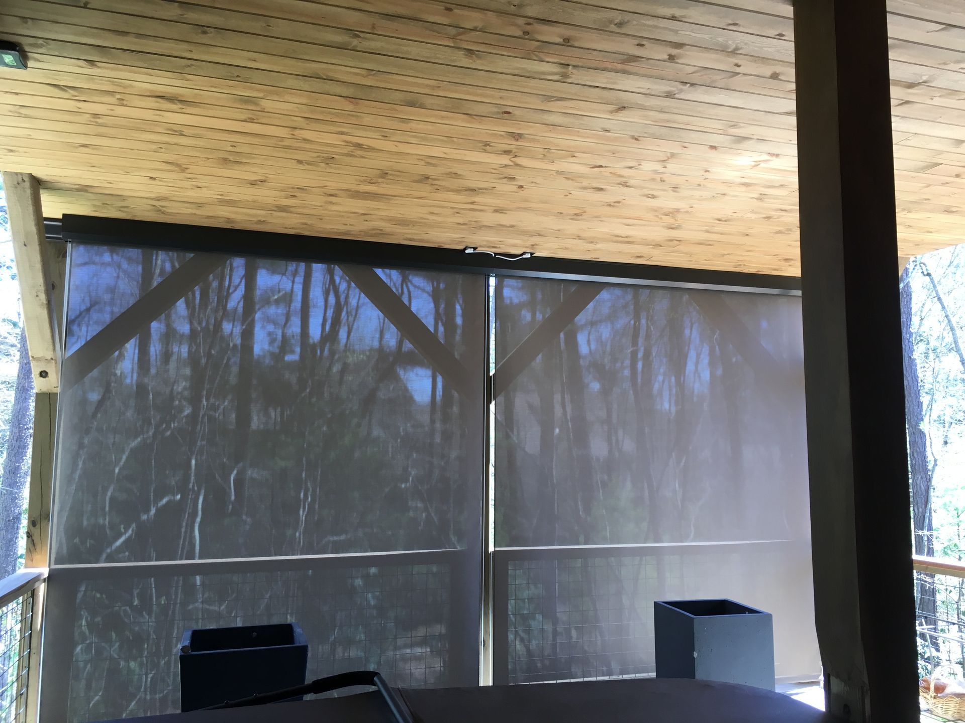 Covered outdoor patio with a woven wood ceiling, dark mesh screen walls, and a wooden support post.