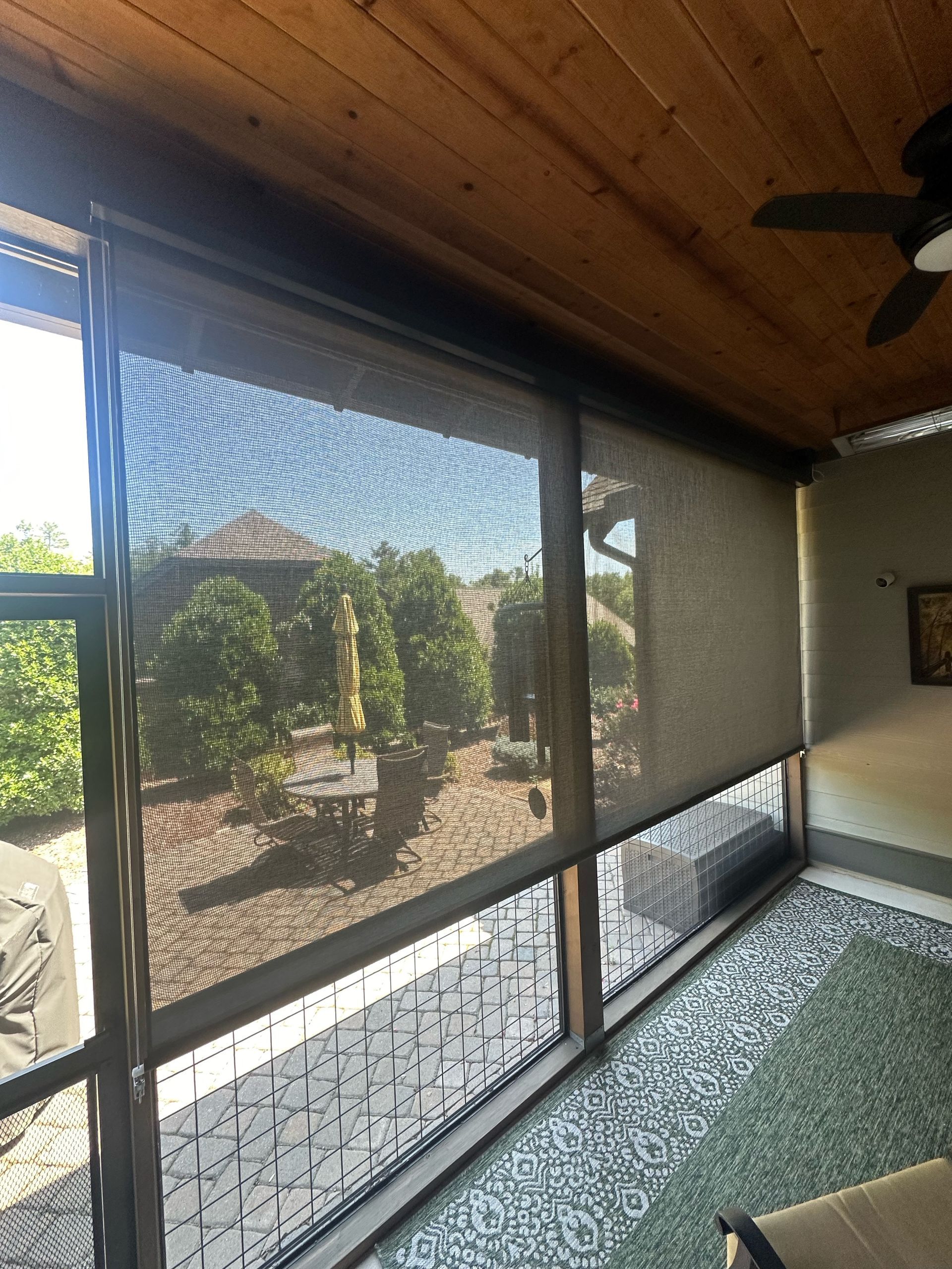 Screened porch with wood ceiling, tiled floor, and view of patio and garden outside.