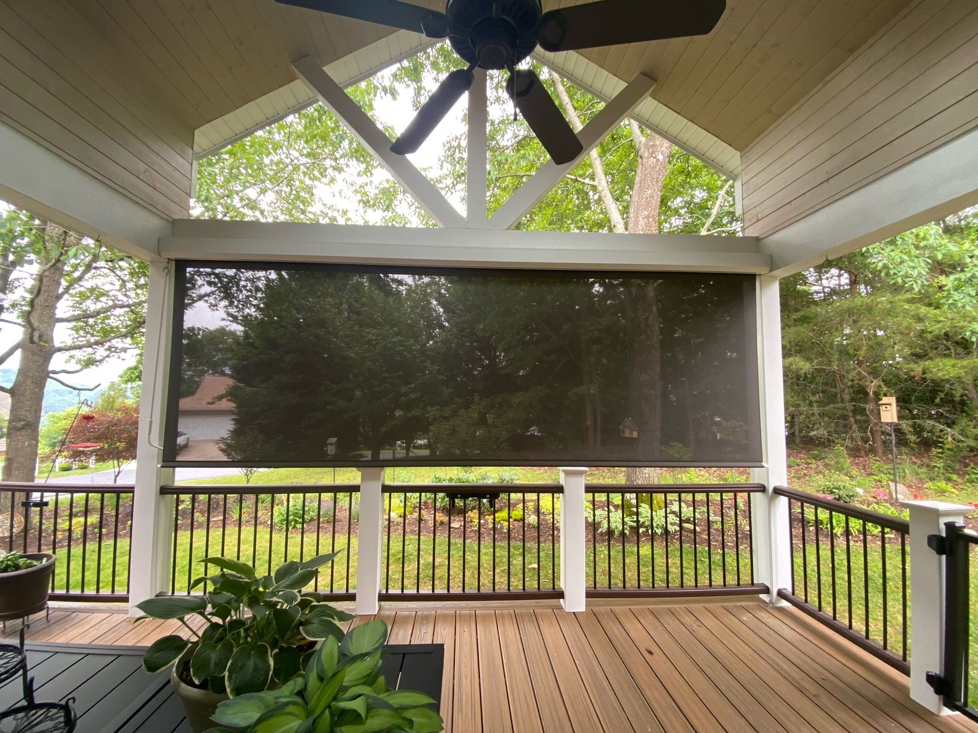 Covered porch with a large screened opening, wooden floor, ceiling fan, and potted plants overlooking a yard