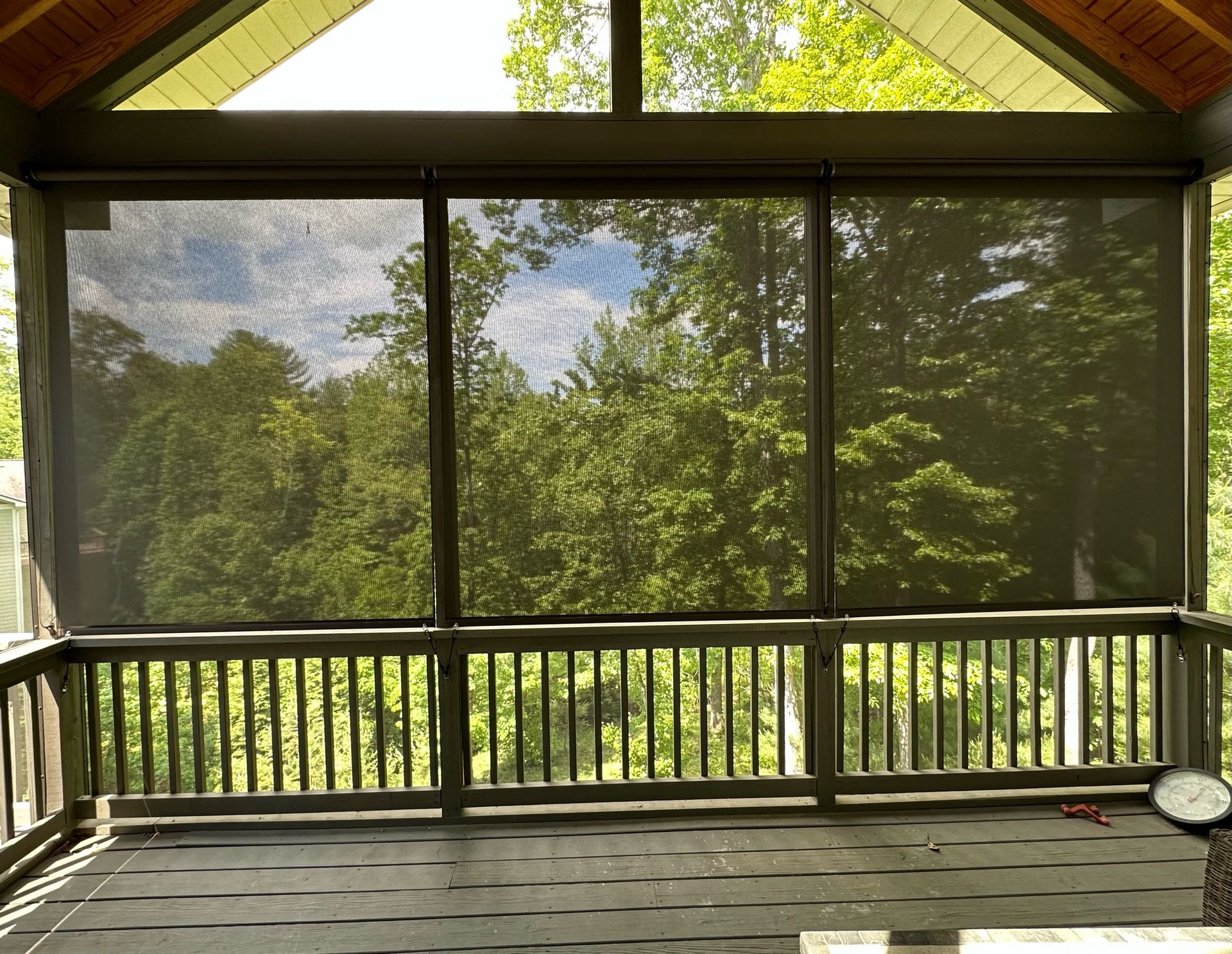 Screened porch with wooden railing overlooking a green wooded yard