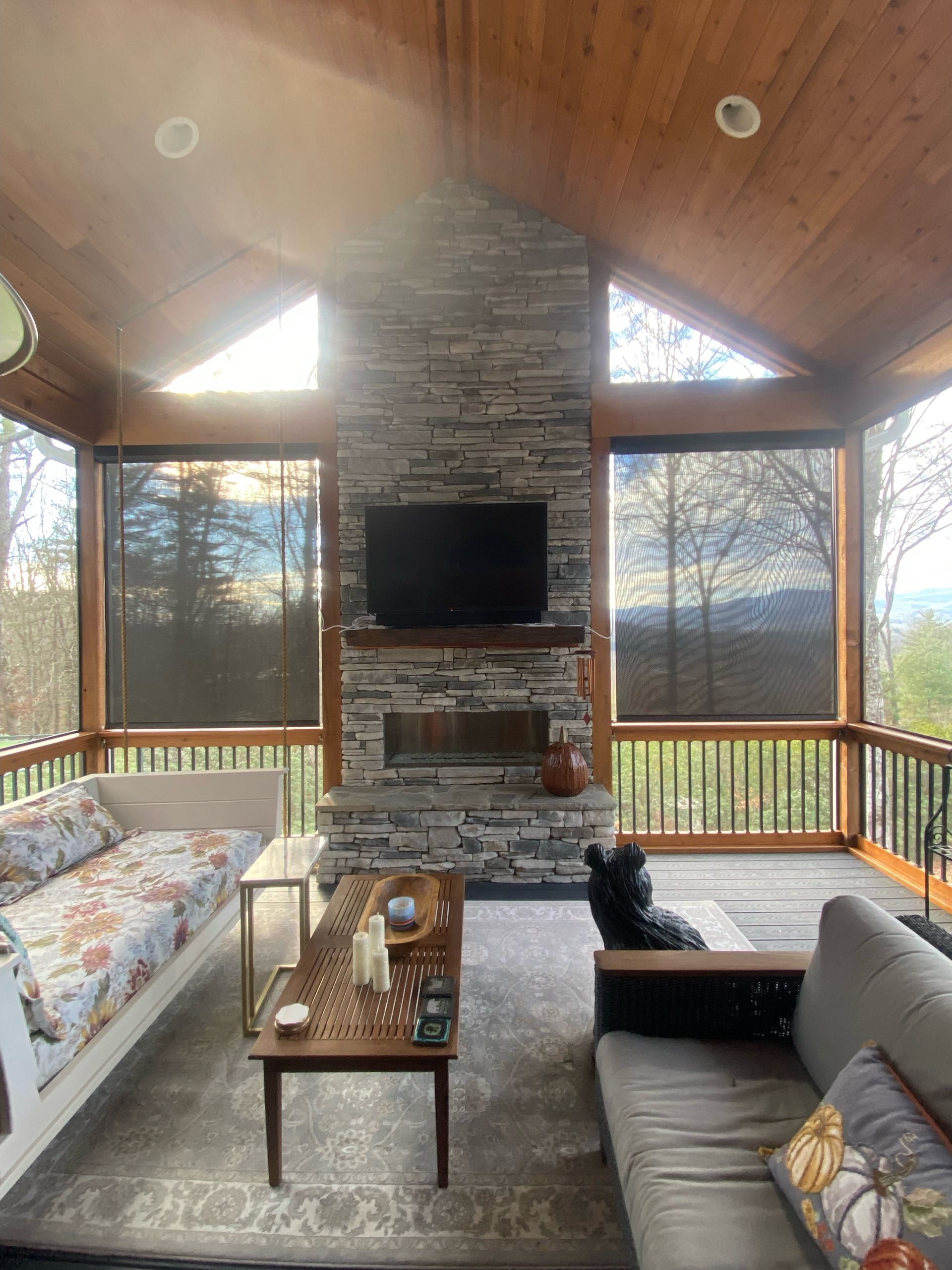 Cozy screened porch with stone fireplace, sectional so fa, coffee table, and forest view.