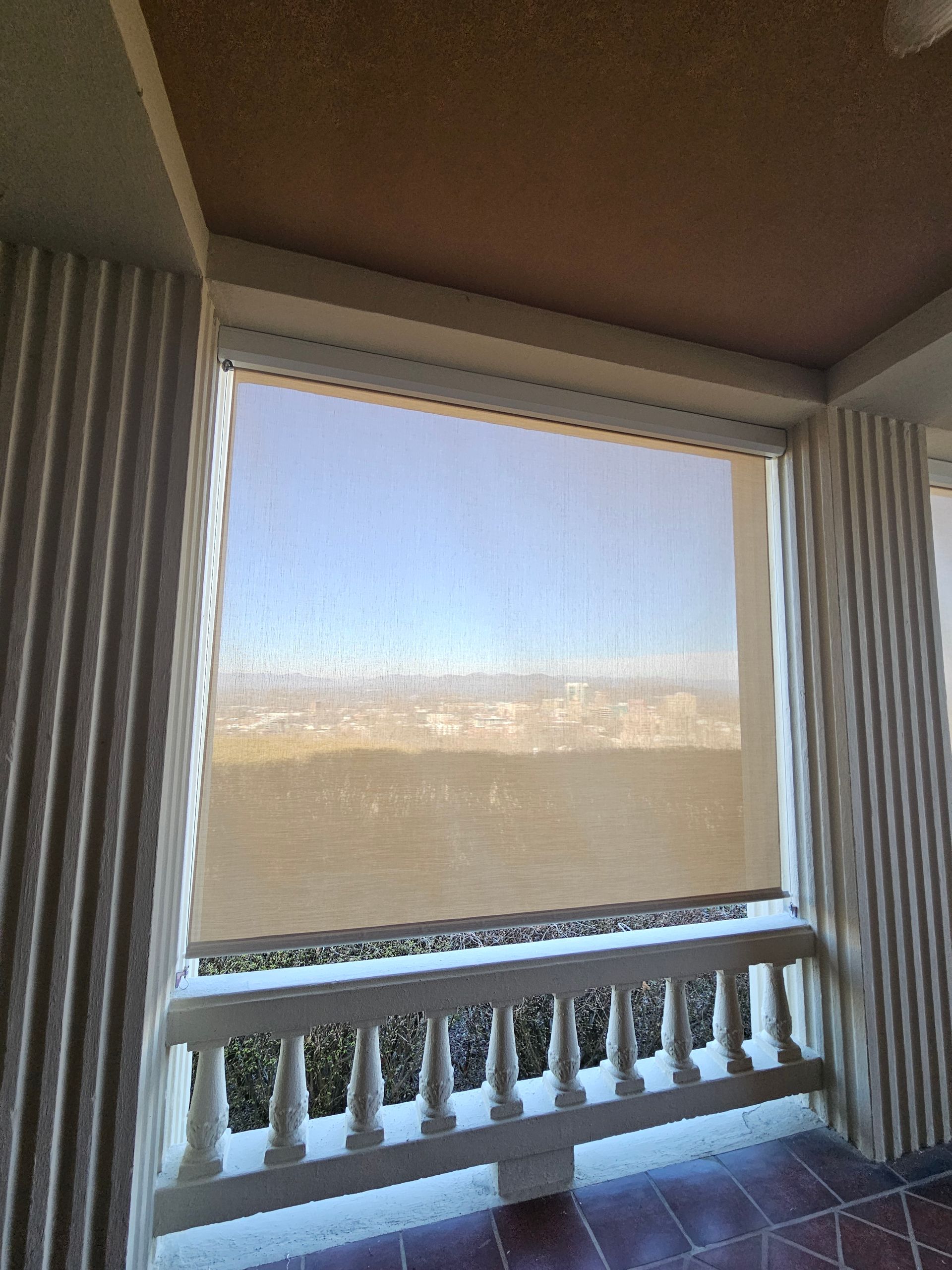 Sliding glass door with frosted lower panel and vertical blinds, looking out to a sunlit view of buildings and sky
