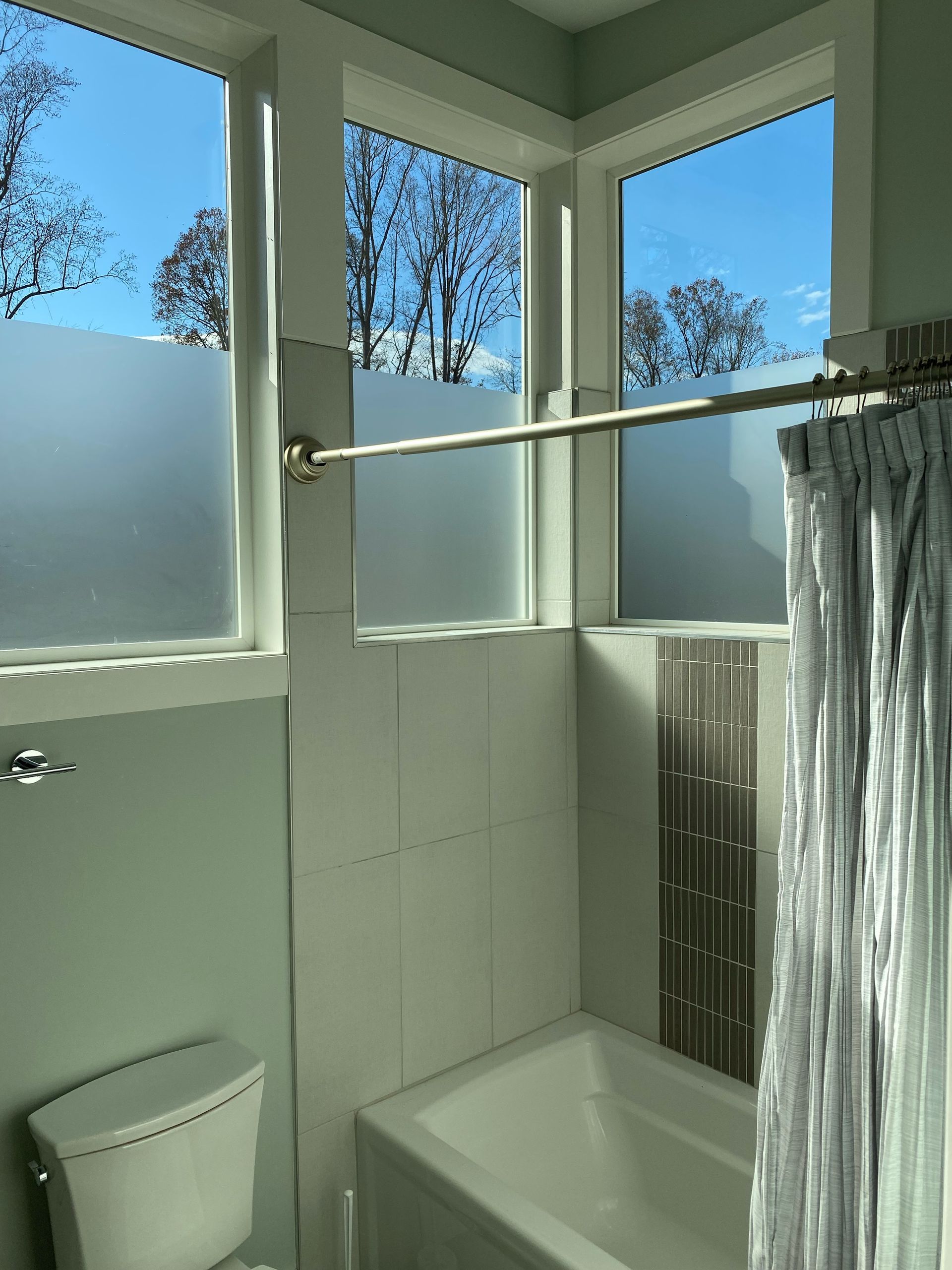 Small bathroom with frosted window, shower curtain, bathtub, and toilet in daylight.