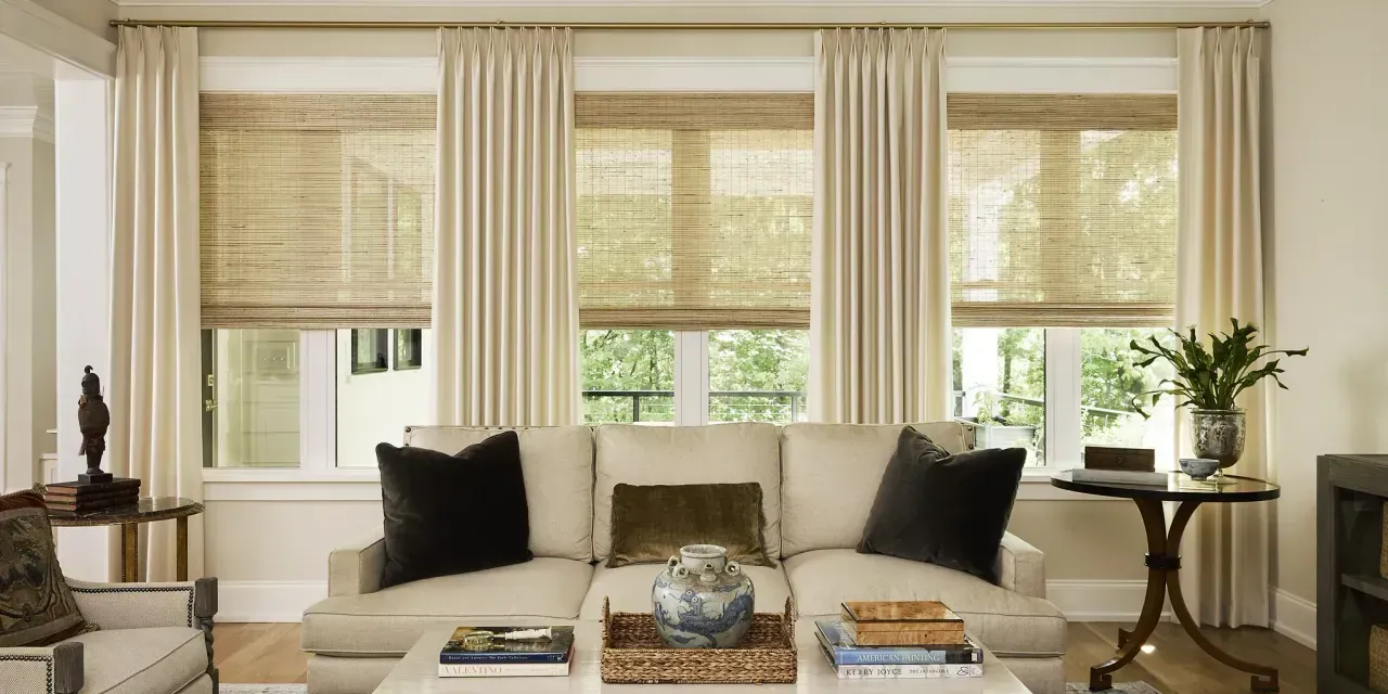 Living room with light beige sofa, curtains, and woven shades on the windows.
